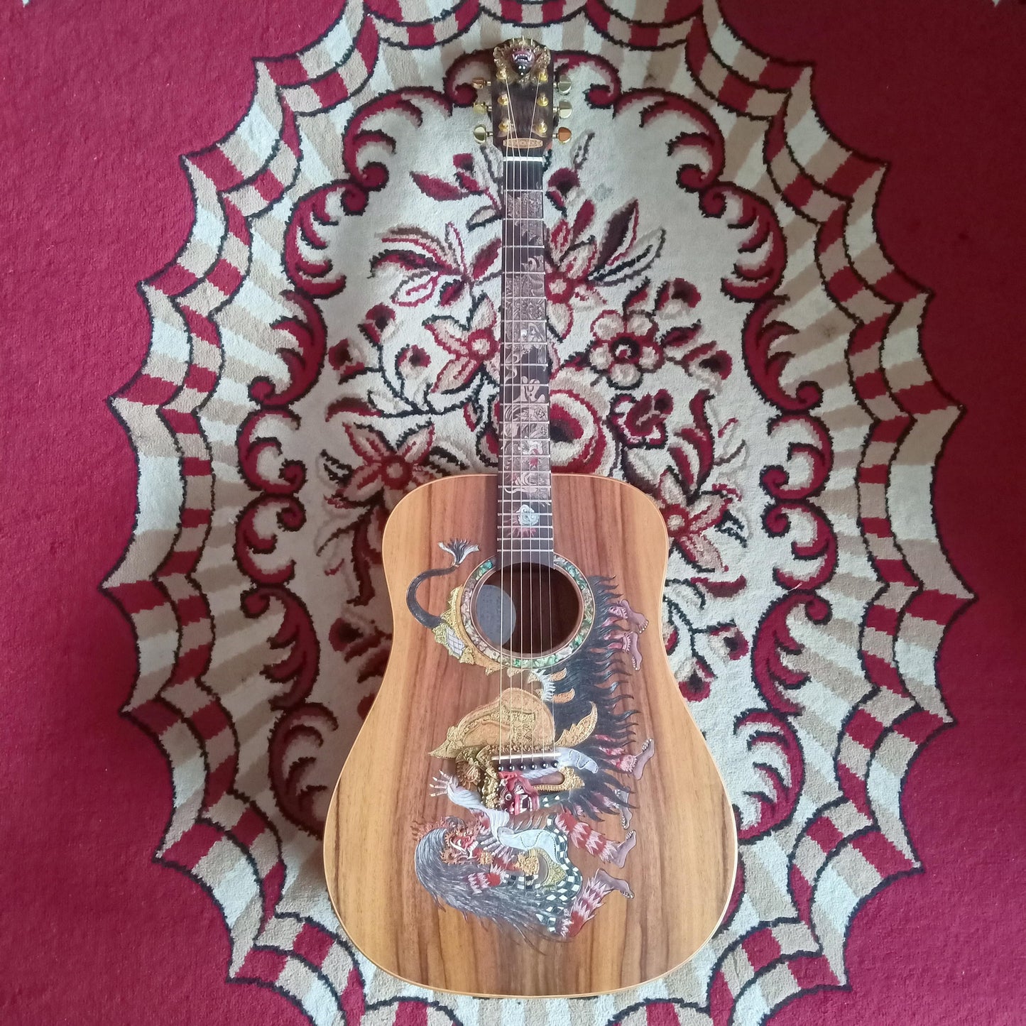 The Blueberry Barong guitar placed on a red carpet, showcasing colorful Barong artwork on the body.