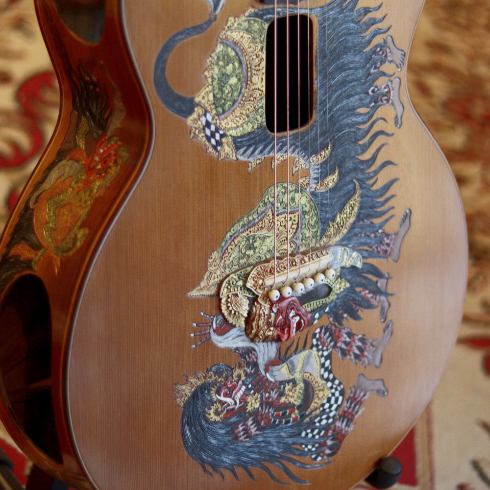 A close-up of an acoustic guitar with an intricate and colorful barong rangda design painted on the body.