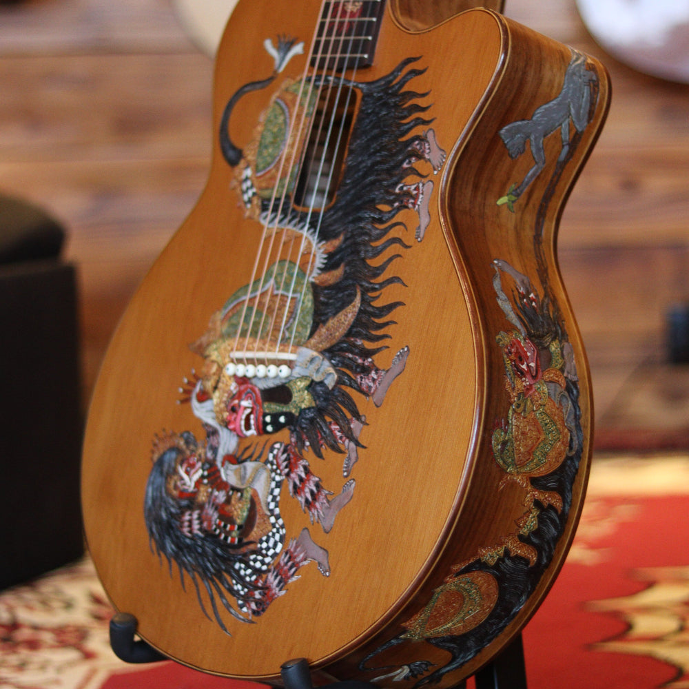 A wooden guitar with colorful Barong and Rangda artwork on the body and side.