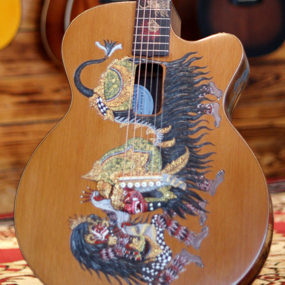 A wooden guitar with detailed Barong and Rangda artwork on the front body