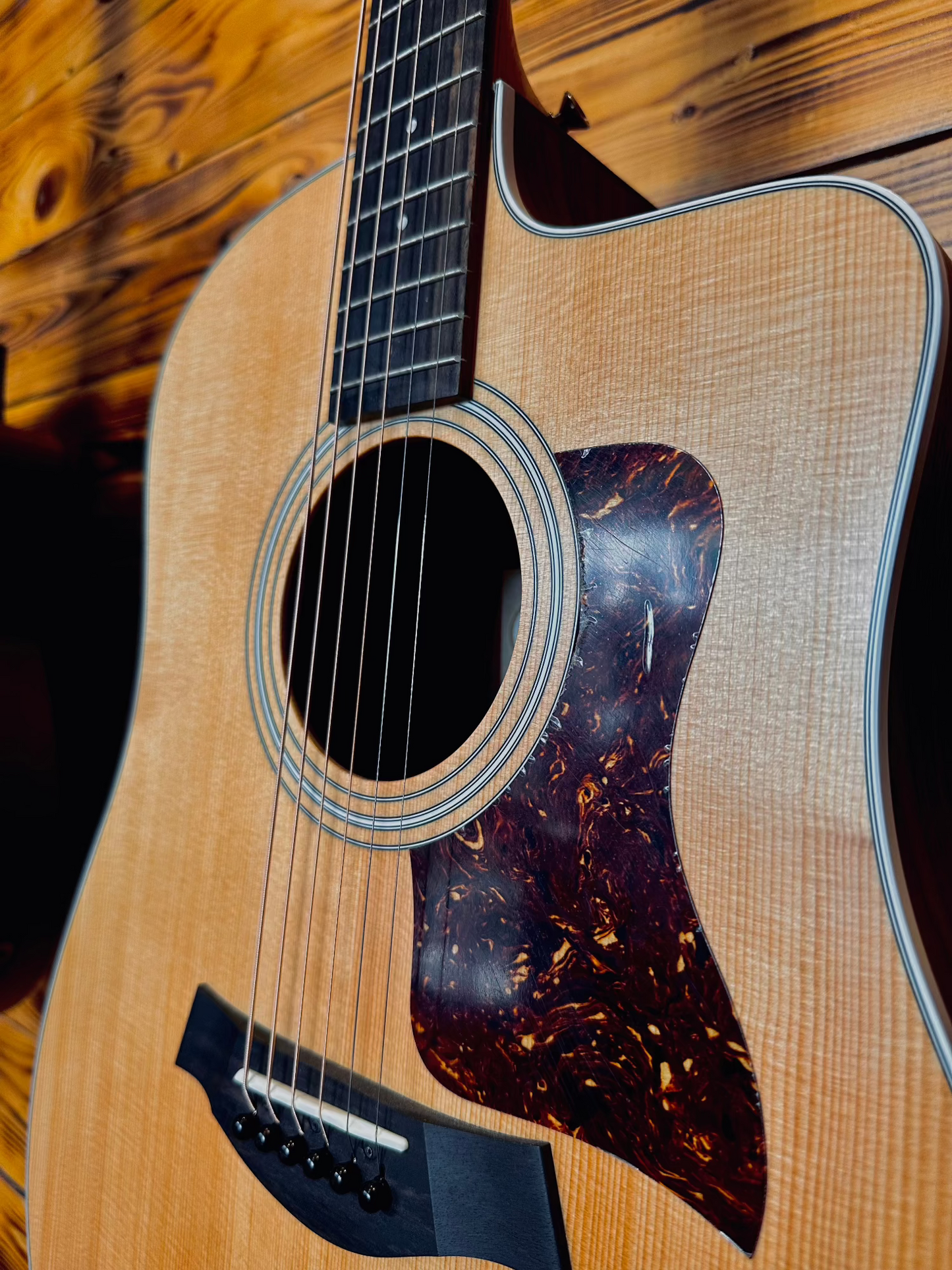 Close-up of the front body of a Taylor 210CE acoustic guitar, highlighting the pickguard and spruce top.