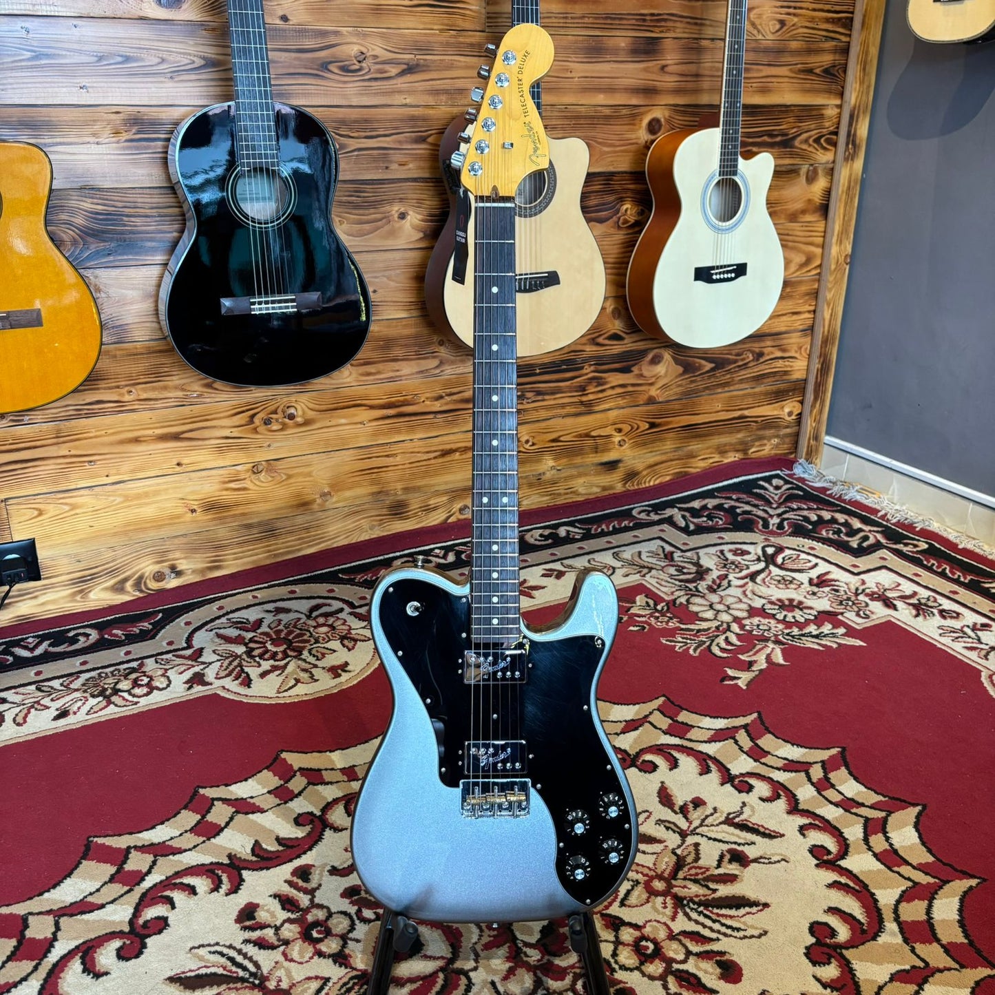 A Fender American Pro II Telecaster Deluxe guitar with a glossy finish, maple neck, and rosewood fingerboard, displayed in a store among other guitars.