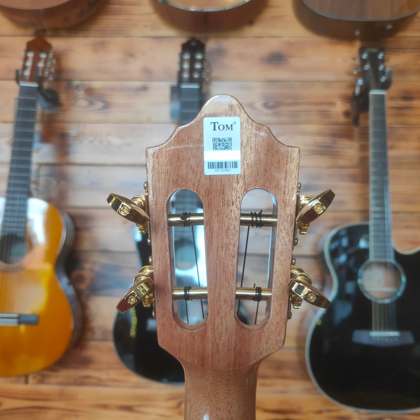 Back headstock of a TOM ukulele, showing tuning pegs and a barcode sticker.