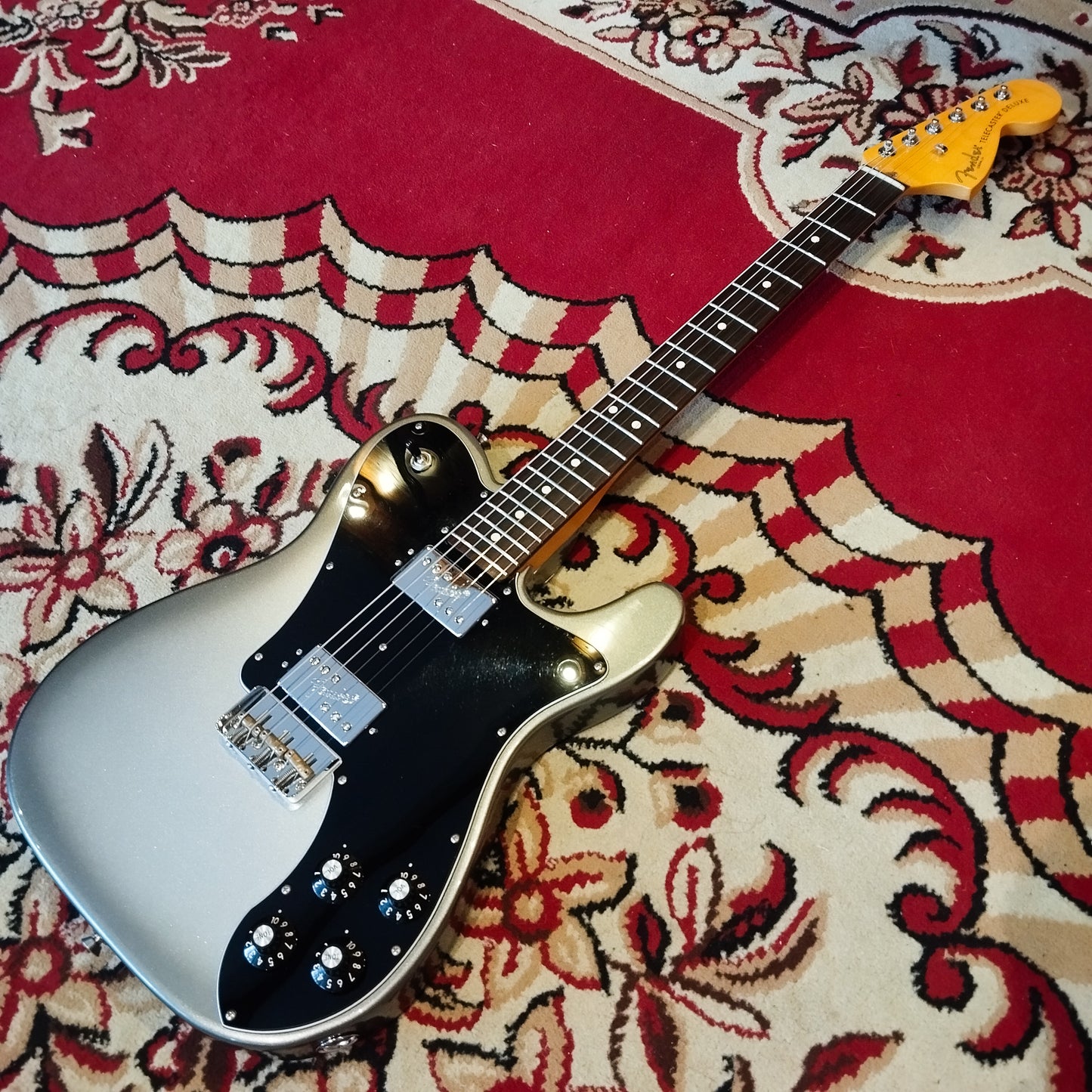 A Fender American Pro II Telecaster Deluxe electric guitar lying on a red carpet, showing its full body and classic design