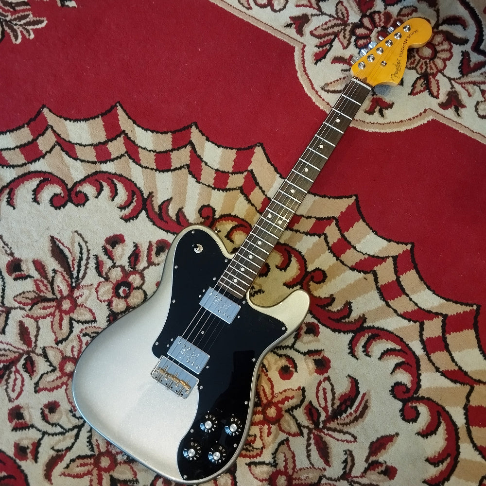A Fender American Pro II Telecaster Deluxe electric guitar lying on a red carpet, showing its full body and classic design.