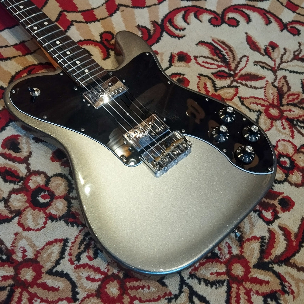 The front body of a Fender American Pro II Telecaster Deluxe electric guitar on a red carpet, featuring dual humbuckers and a sleek finish.