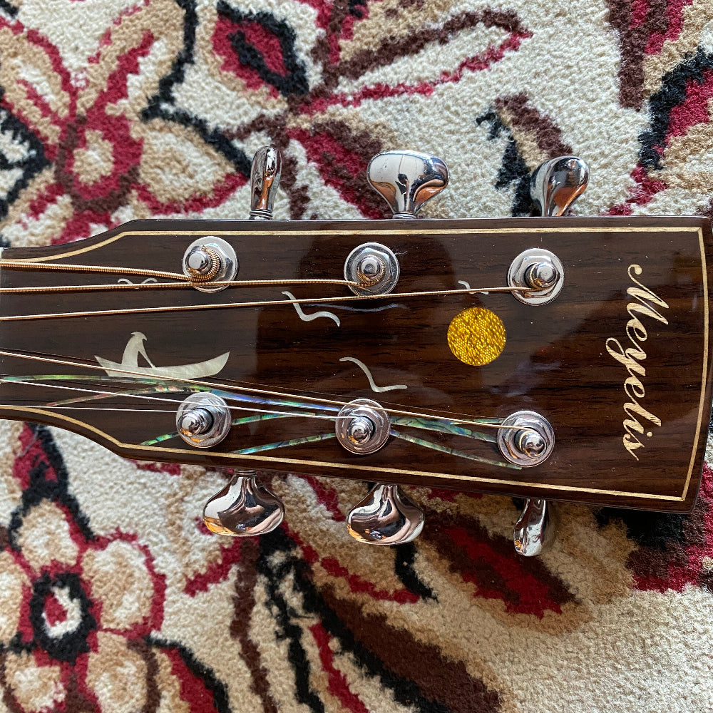 Guitar headstock with 'Meyelis' branding on a patterned surface