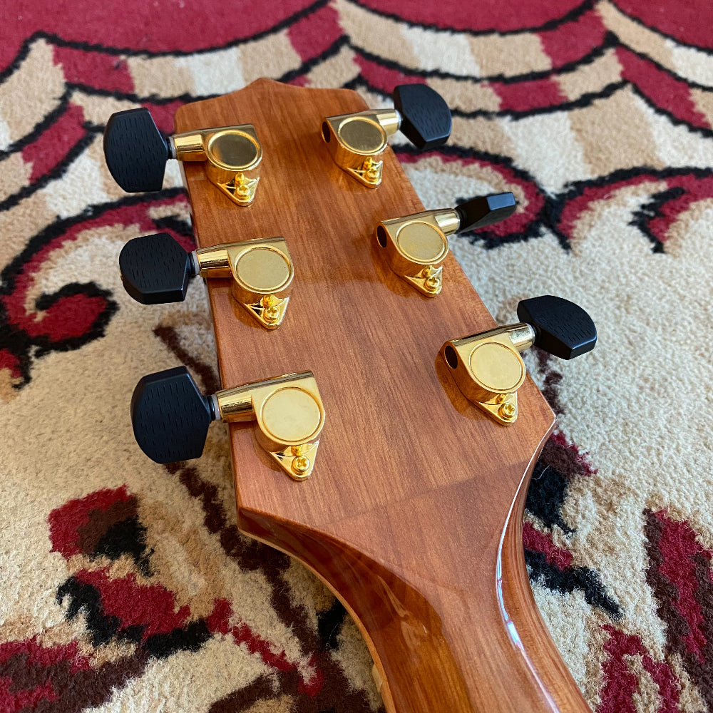 Guitar headstock with gold tuning pegs on a patterned rug