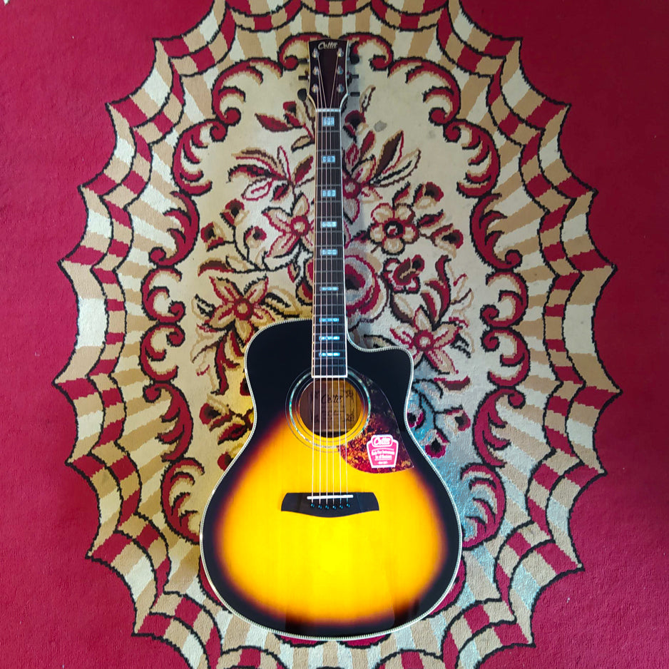 An acoustic guitar Cetta LV33SCE in TVS color resting on a red carpet, featuring a sunburst finish and cutaway design.