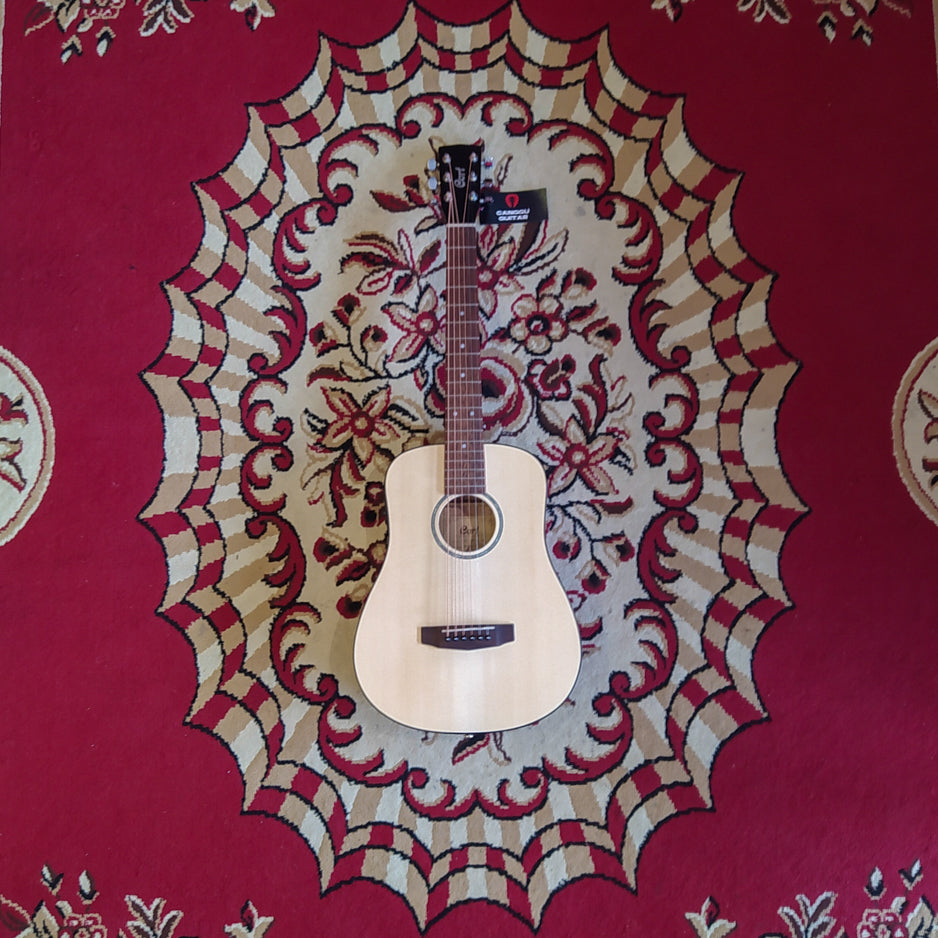 A Cort Mini Series acoustic electric guitar with a solid Adirondack spruce top and mahogany back and sides, displayed on a patterned red and beige backdrop.