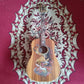The Blueberry Barong guitar placed on a red carpet, showcasing colorful Barong artwork on the body.