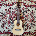 A TOM ukulele resting on a red carpet, showing its wooden body and classic design.