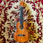 A tenor ukulele resting on a red carpet, showing its wooden body and classic design