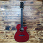 A Cetta OM28CE acoustic guitar resting on a wood wall, featuring a red wood finish and cutaway design.